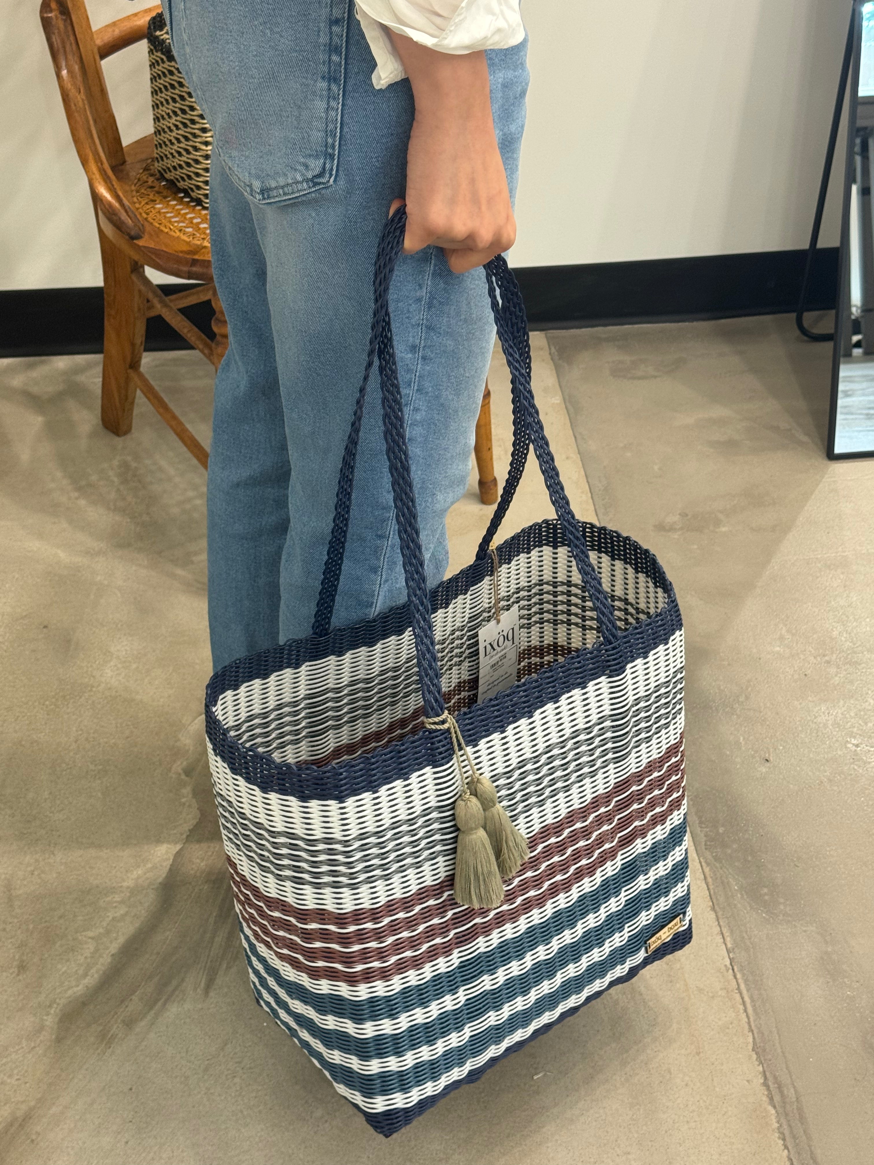 Person holding a striped tote bag with blue, white, and brown colors.