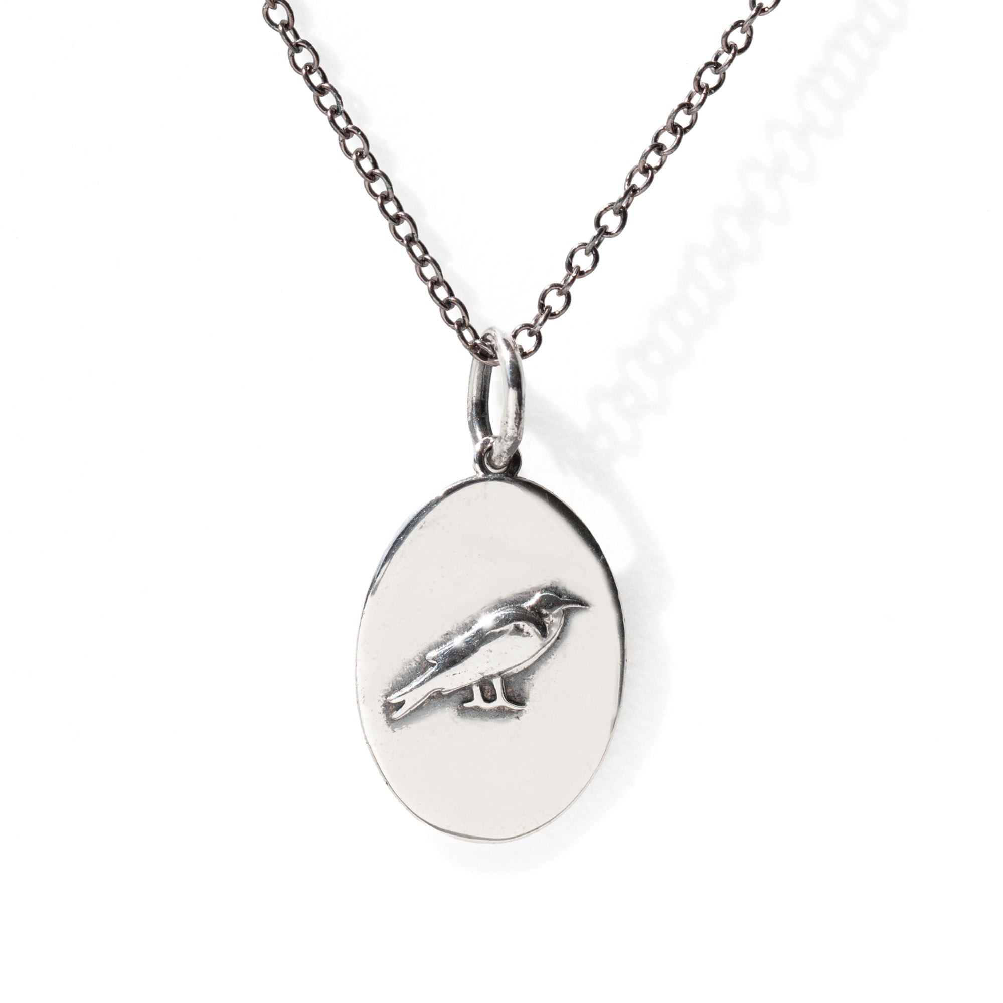 Silver necklace with oval pendant featuring a bird design on a white background