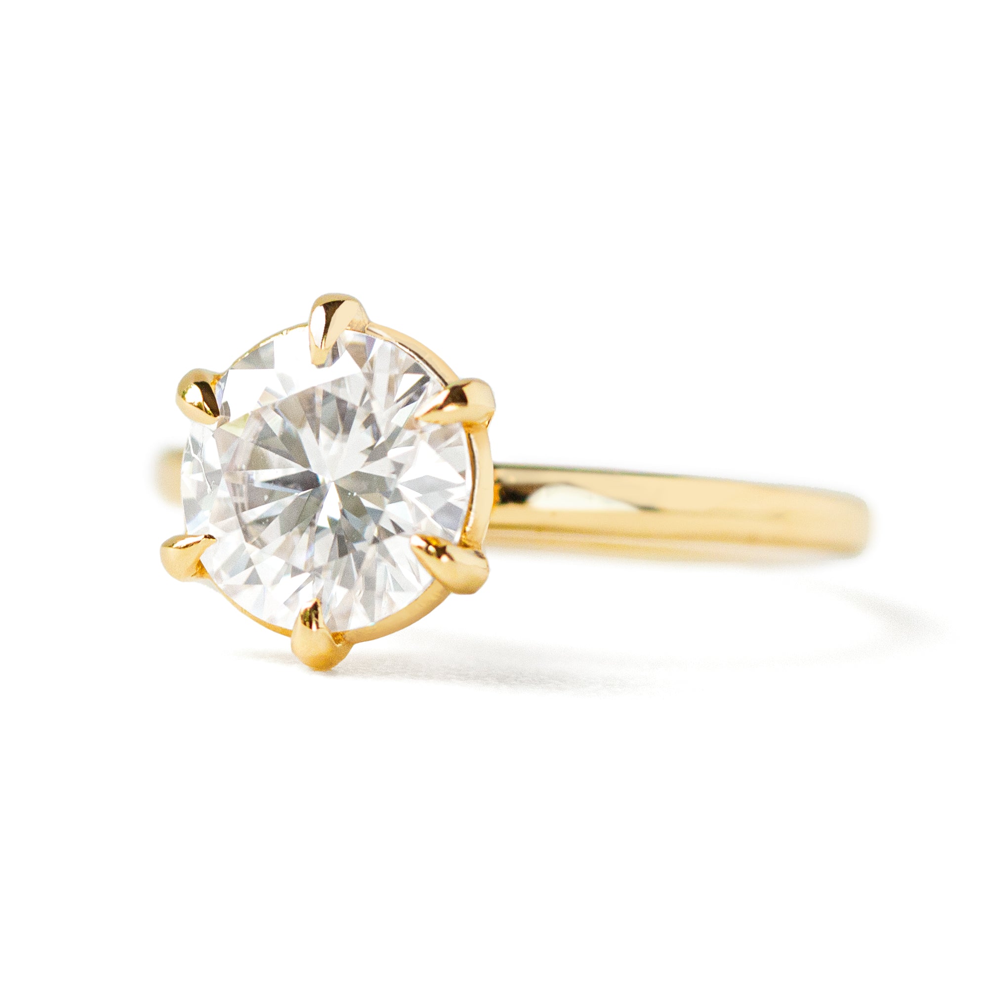 A gold solitaire ring with a round center diamond held by six prongs.