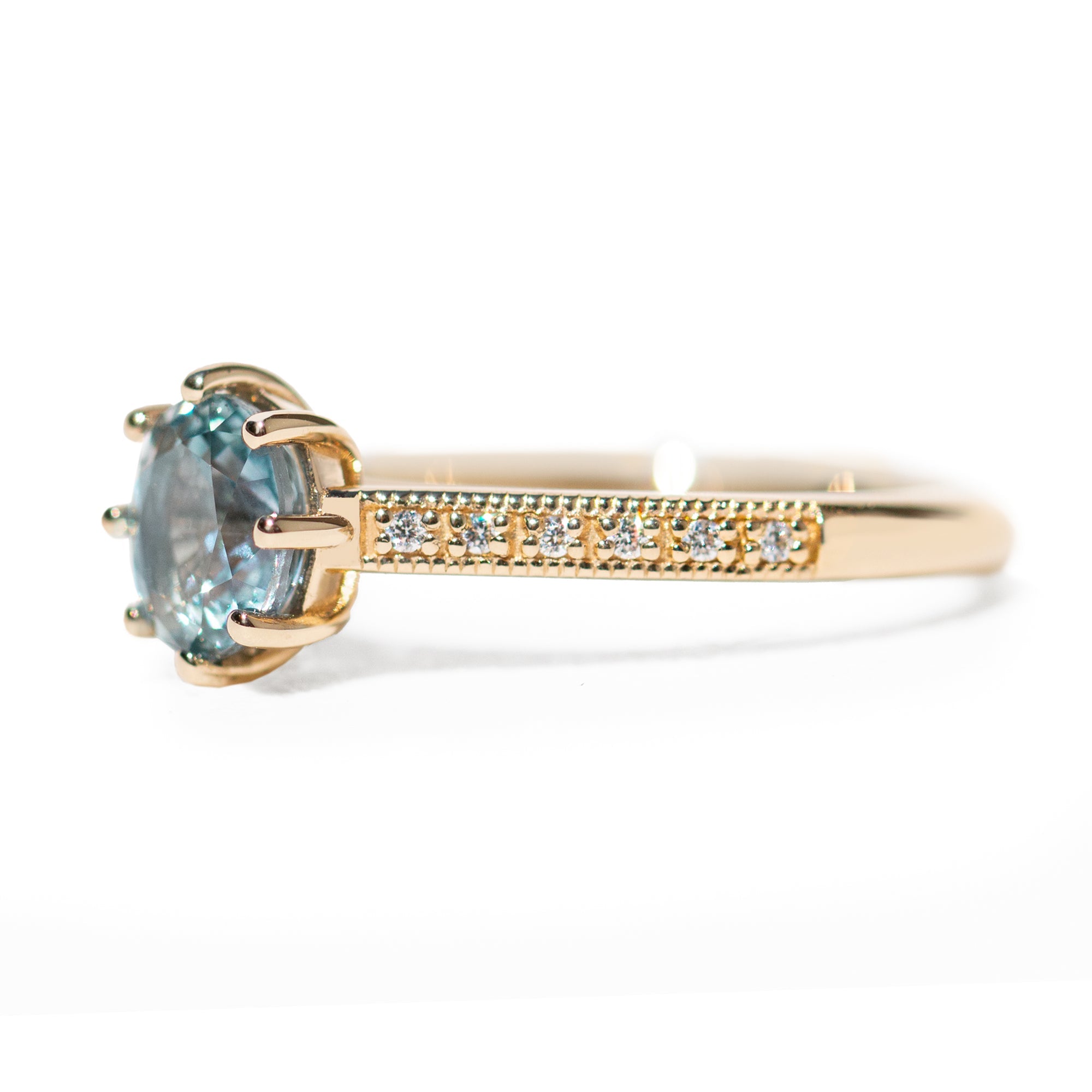 Gold ring with a blue gemstone and diamond-studded band on a white background