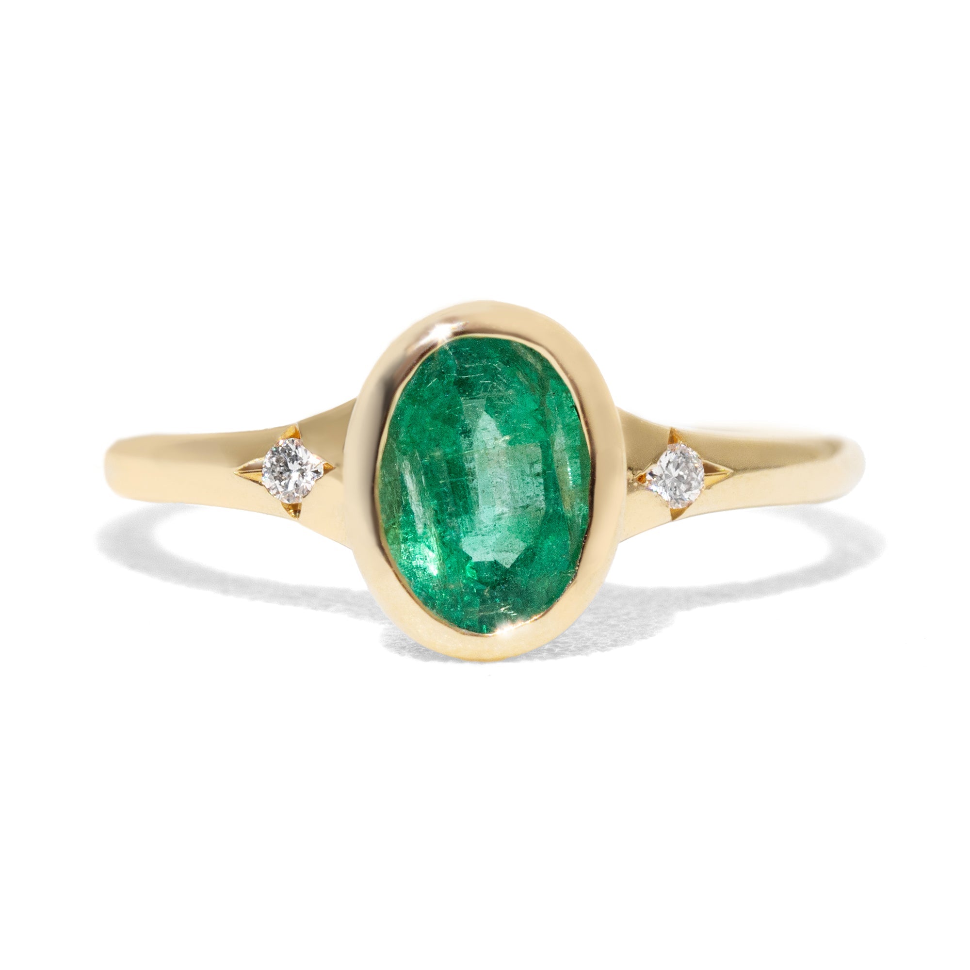 an oval emerald set gold ring and a contour gold band accented with thre diamonds on white background.