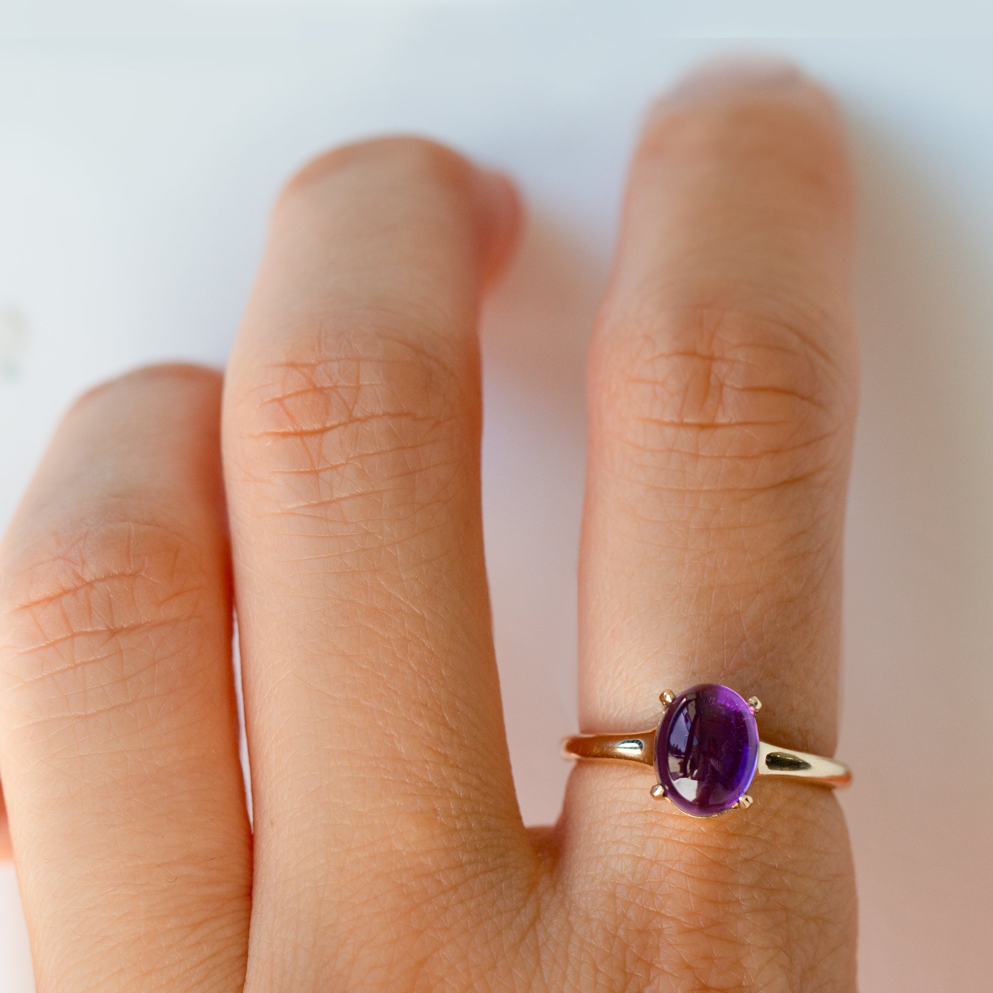 Gold ring with a purple gemstone on a person's finger against a white background