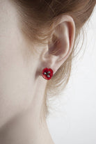Close-up of a person wearing a red flower-shaped earring on a plain background