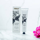 Shea butter hand and body crème with packaging on a marble surface, featuring a pink flower.