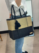 Person holding a black and beige woven tote bag with tassels.