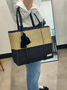 Person holding a black and beige woven tote bag with a tassel.
