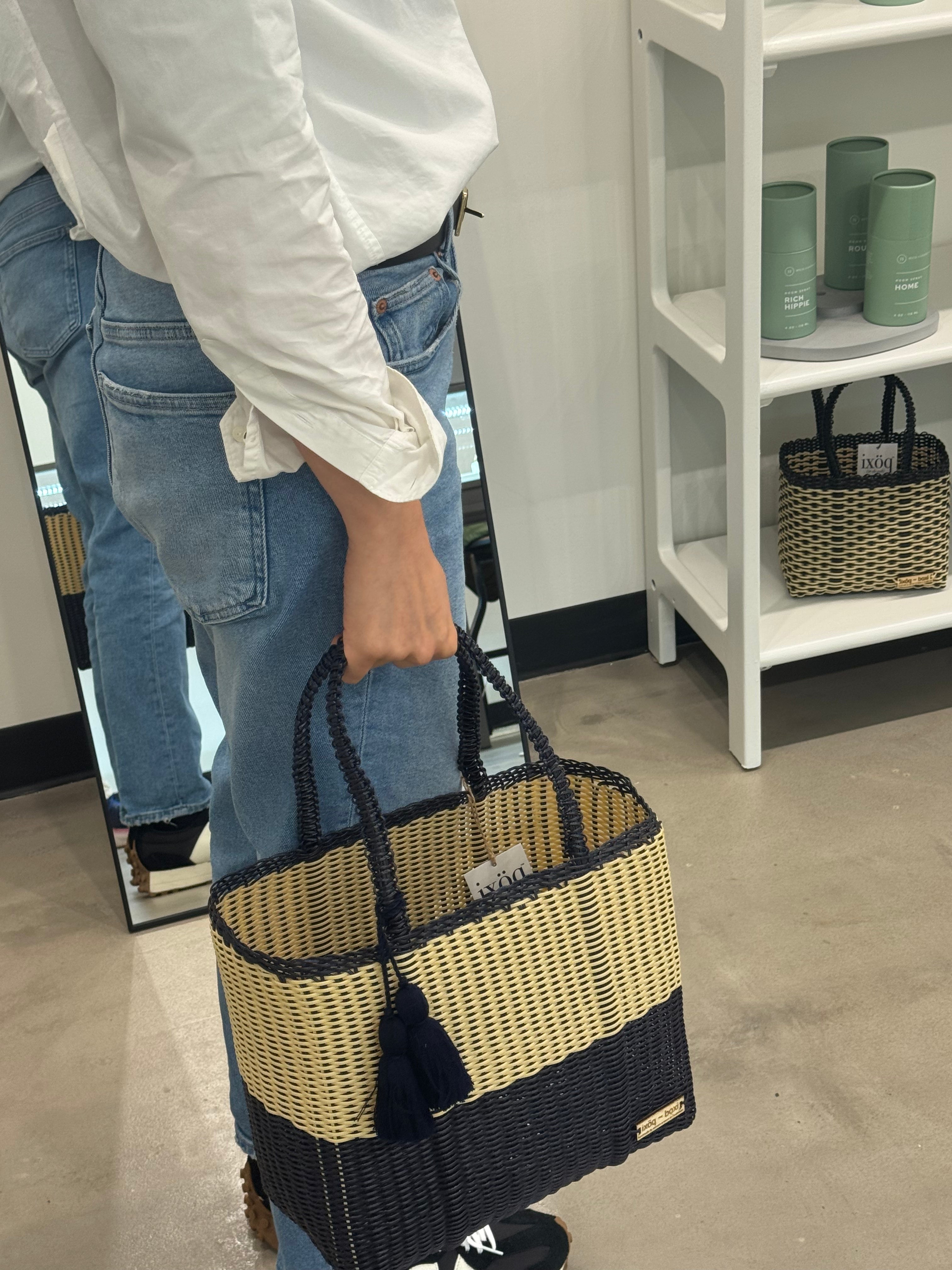 Person holding a woven handbag with a mirror and shelves in the background