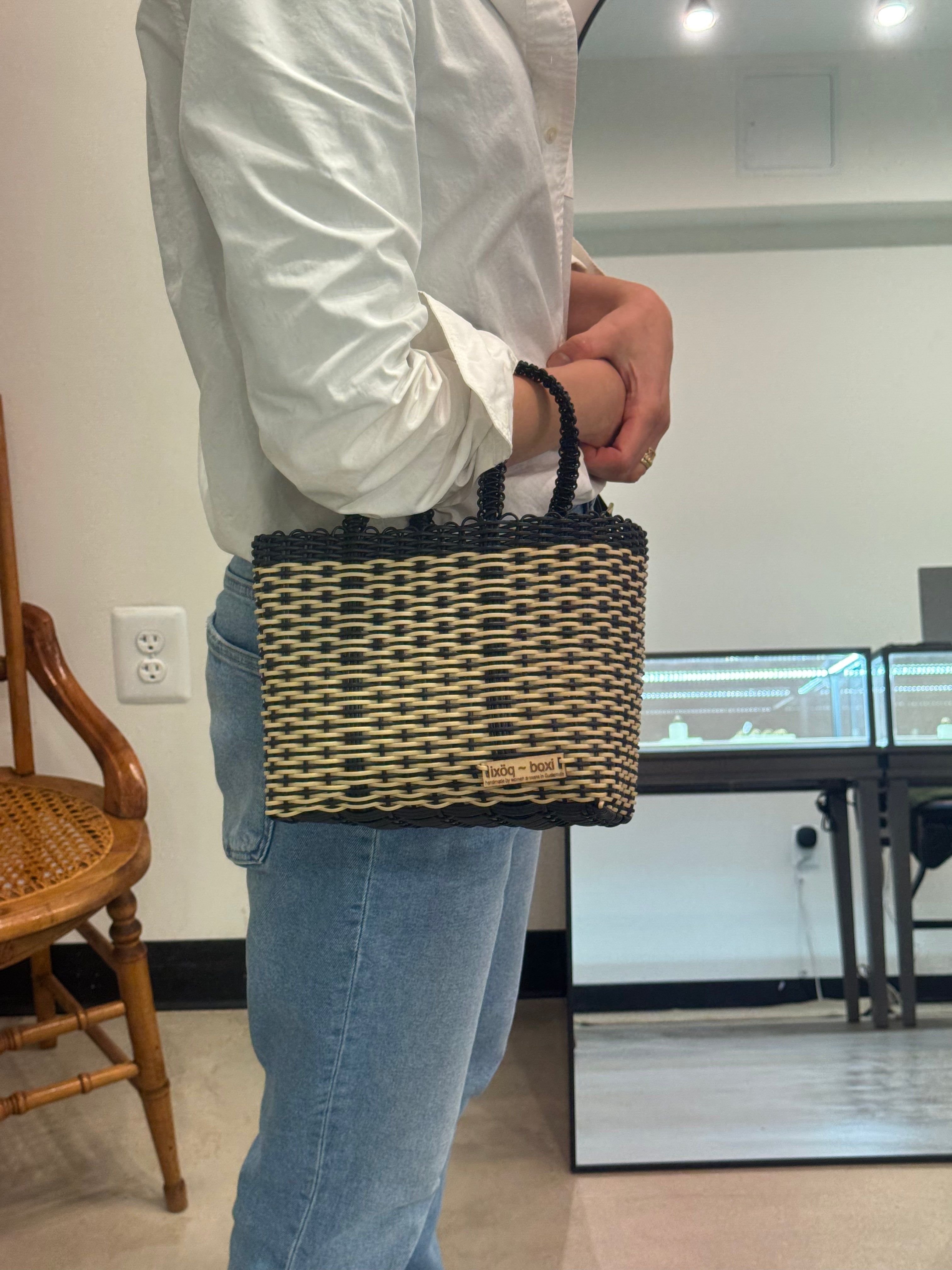 Person holding a woven handbag in an indoor setting