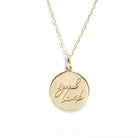 Gold necklace with a round pendant engraved with 'good luck' on a white background
