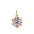 A gold flower-shaped pendant charm featuring a central light blue round gemstone surrounded by six surrounding clear and lavender-purple round gemstones, set against a plain white background.