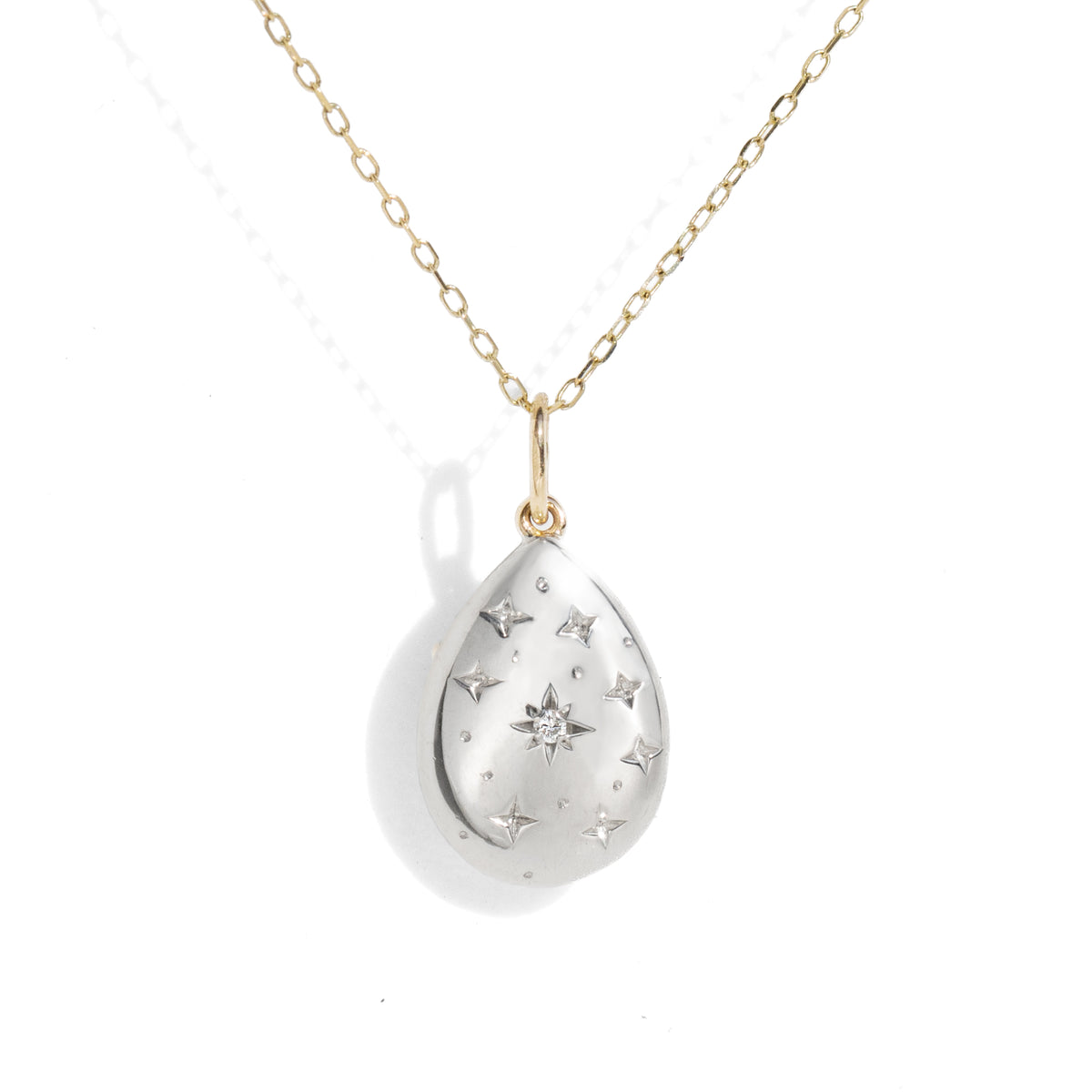 A teardrop-shaped silver pendant necklace with a gold chain, featuring a central diamond and star engravings, set against a plain white background.