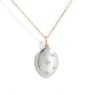 A silver oval pendant necklace with a gold chain, featuring a central starburst design and small star accents, shown on a plain white background.