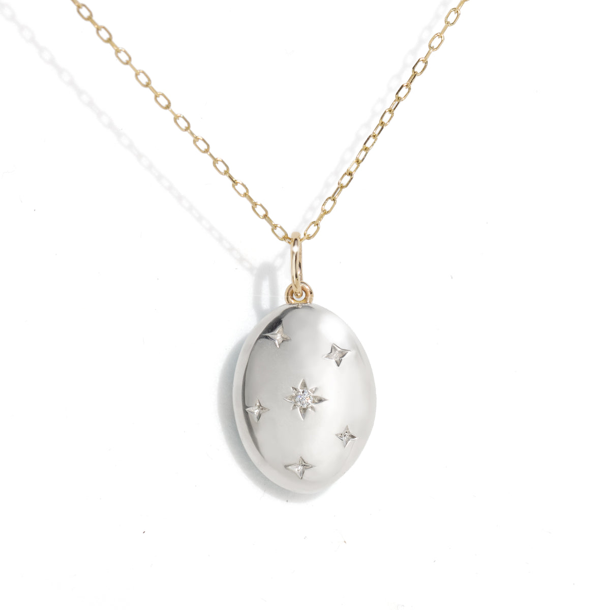 A silver oval pendant necklace with a gold chain, featuring a central starburst design and small star accents, shown on a plain white background.
