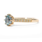 Gold ring with a blue gemstone and diamond-studded band on a white background