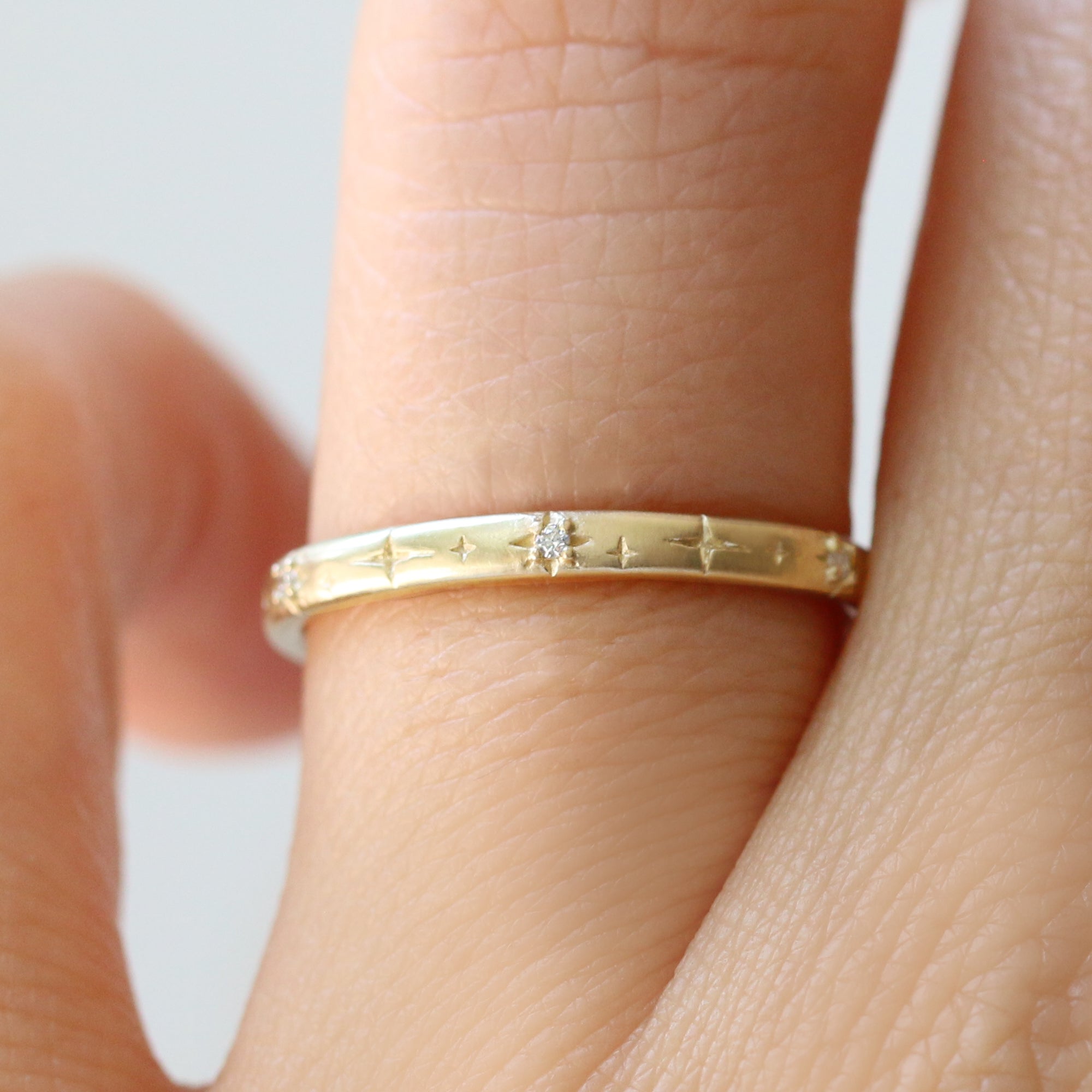 Gold ring with a diamond on a finger against a neutral background
