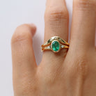 hand wearing an oval emerald set gold ring and a contour gold band accented with thre diamonds on white background. 