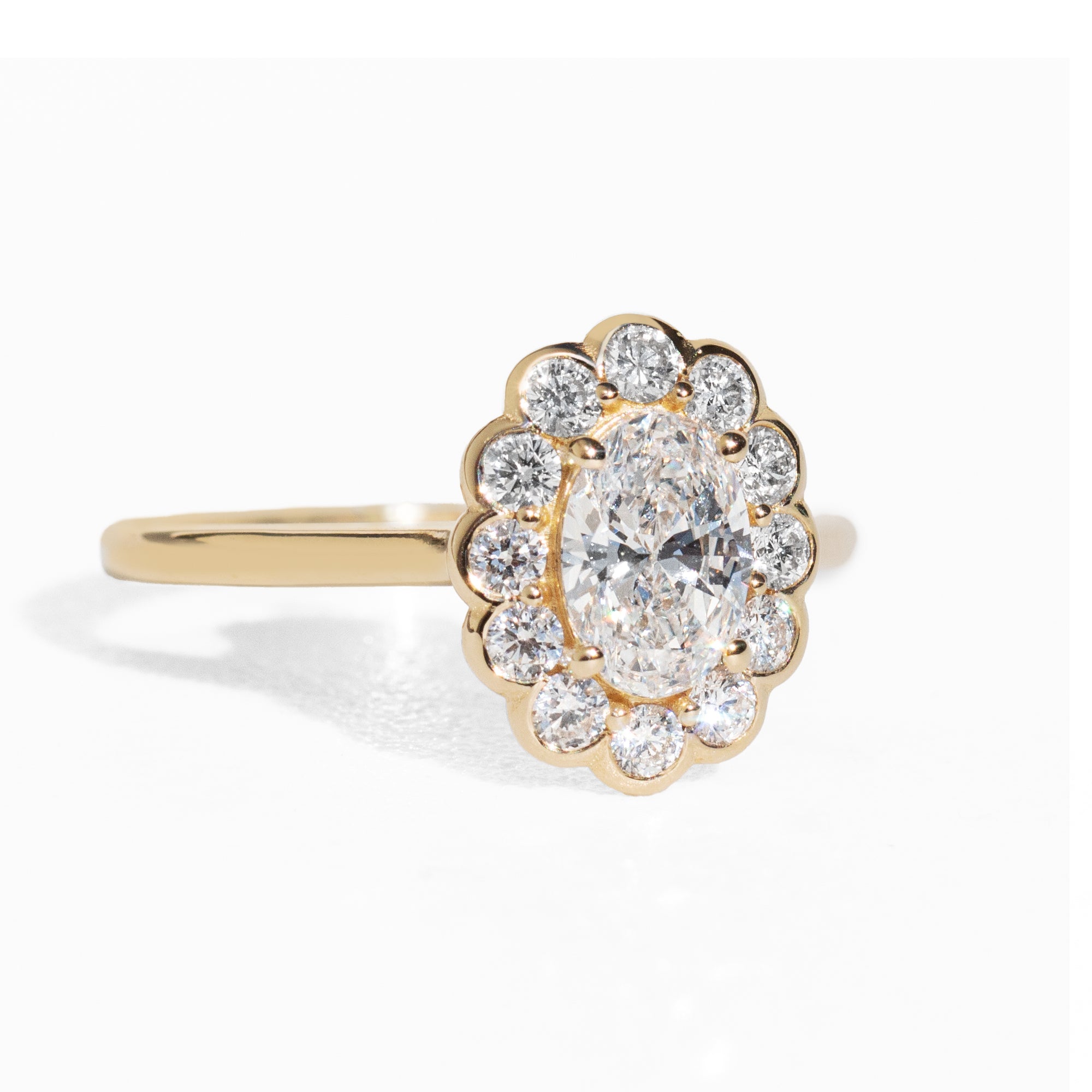 Gold ring with an oval diamond with a halo on a white background