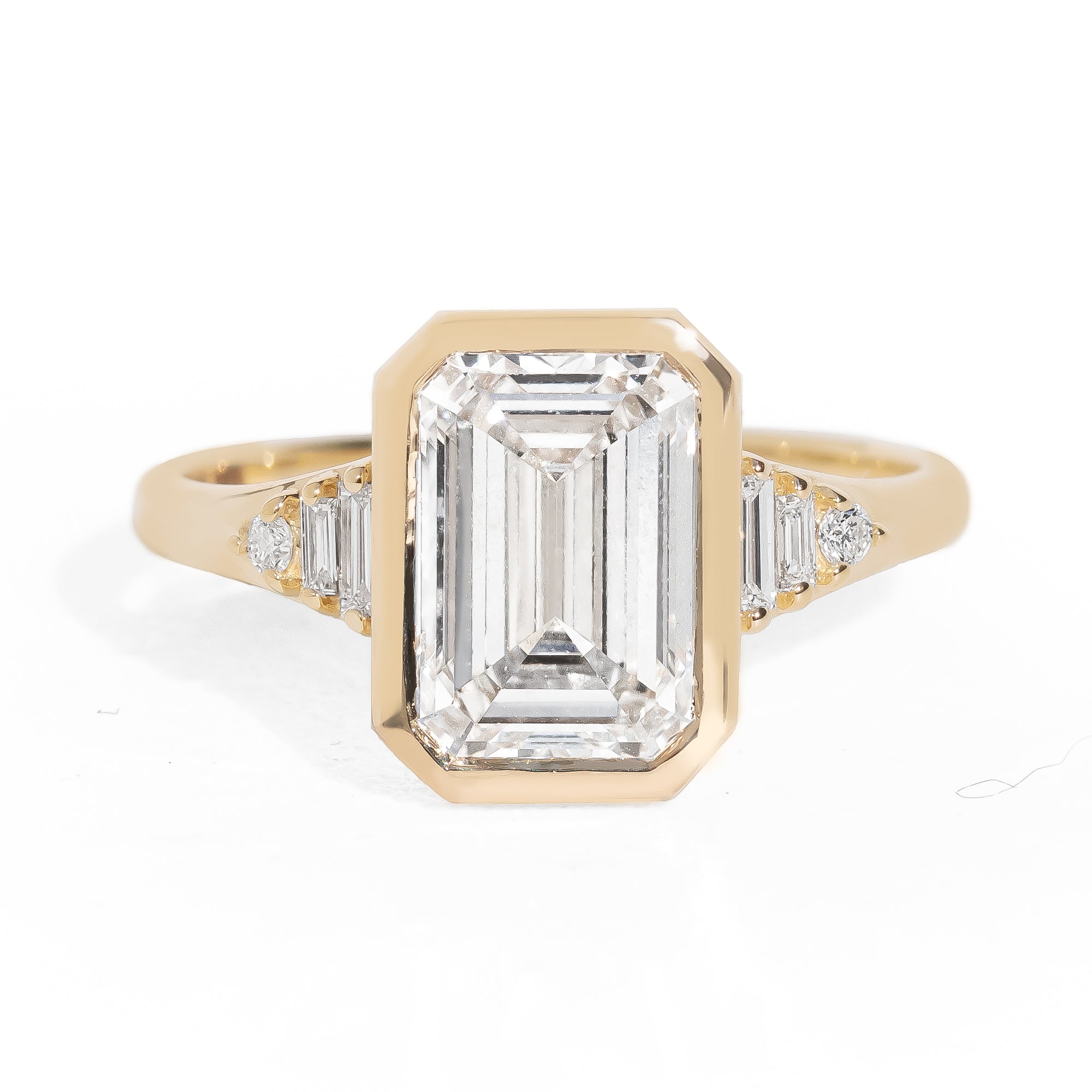Gold ring with emerald-cut diamond and baguette diamonds on a white background