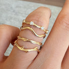 Gold rings with diamond accents on a finger against a neutral background