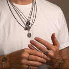 Person wearing multiple necklaces and rings on a plain background