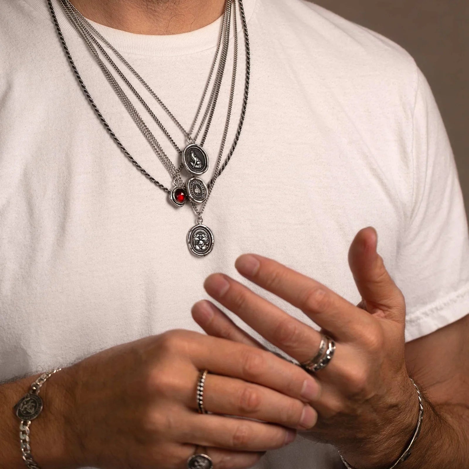 Person wearing multiple necklaces and rings on a plain background