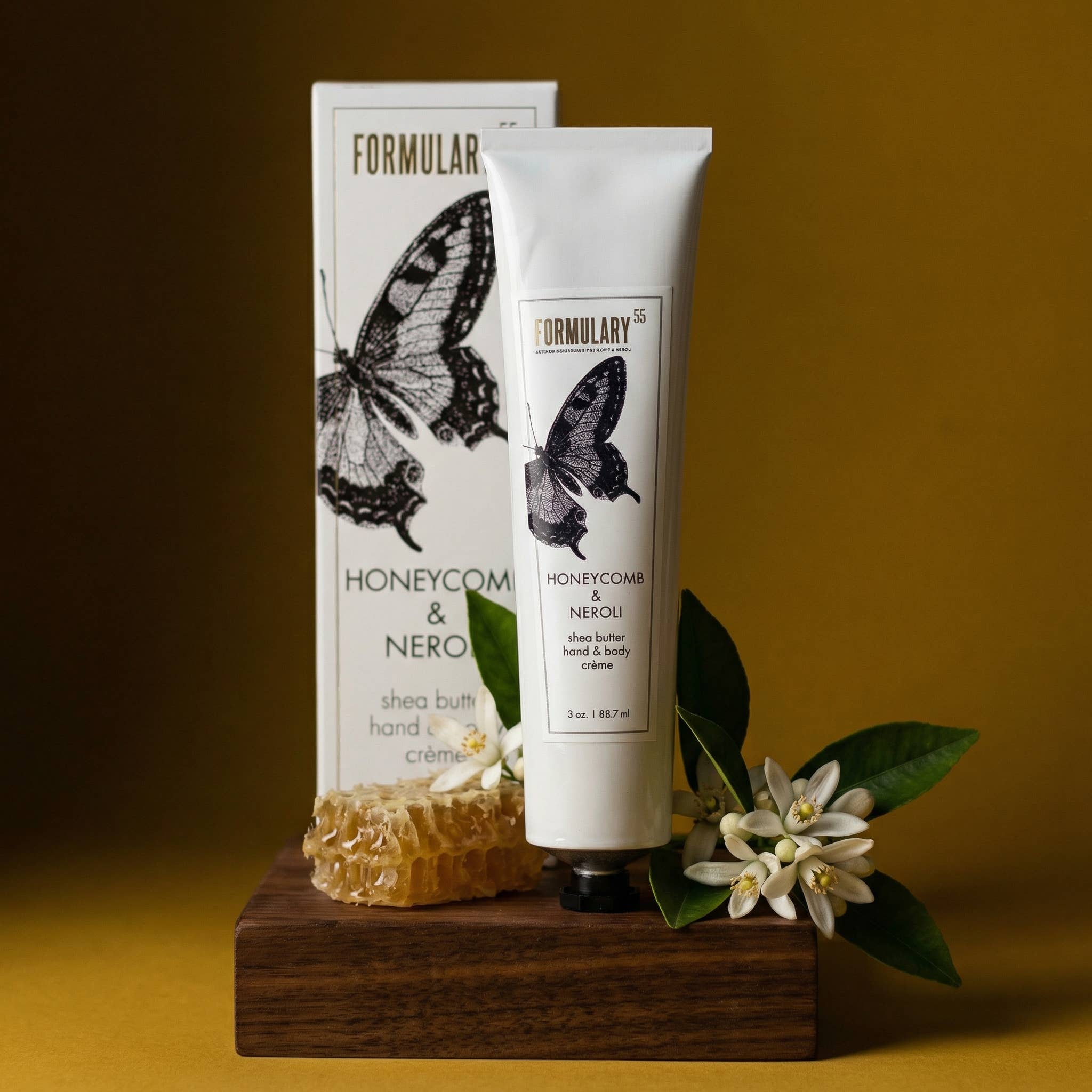 Formulary 55 honeycomb and neroi hand and body cream with packaging on a wooden stand against a yellow background