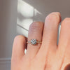 Round diamond ring on a hand against a neutral background. 