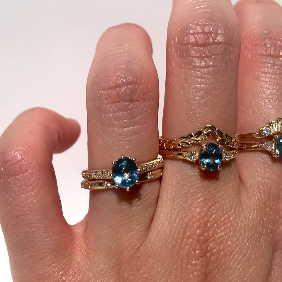 Three teal sapphire rings on a hand against white background. 