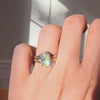 oval diamond engagement ring and a wedding band on a hand against a neutral background