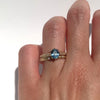 Oval teal color sapphire and a diamond band on a hand against white background. 
