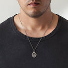 Man wearing a black shirt with a silver necklace featuring a pendant.