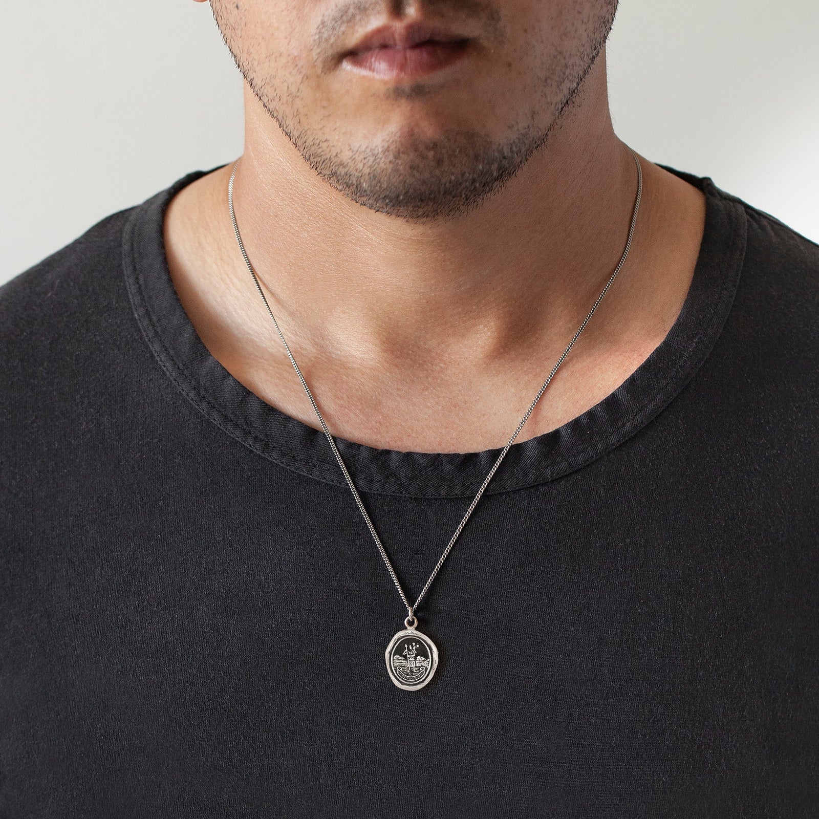 Man wearing a black shirt with a silver necklace featuring a pendant.