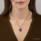 Woman wearing a silver necklace with a pendant against a neutral background