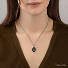 Person wearing a necklace with a black pendant on a plain background