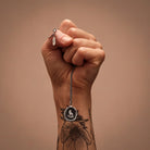 Hand holding a necklace with a pendant against a brown background
